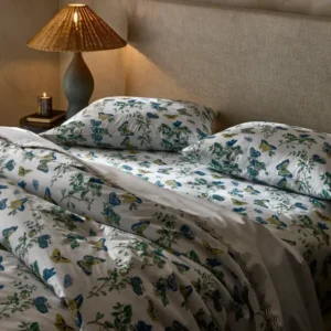 Cozy bedroom featuring a floral butterfly-patterned duvet and pillows, complemented by a warm lamp and candlelight. Featuring Baudin Butterfly printed bedding by Matouk, availabe at Linen Society.