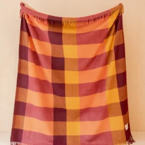 Recycled Wool Blanket in Ochre Bold Check by TBCo displayed hanging with fringed edges on pale wood background