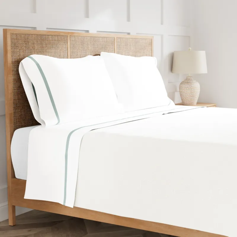 Ann Gish Ready-to-Bed 2.0 white cotton sheet set with sage trim on bed.