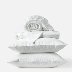 Coyuchi Heirloom Sateen Jacquard sheet set in white, stacked with pillows and rolled fitted sheet.