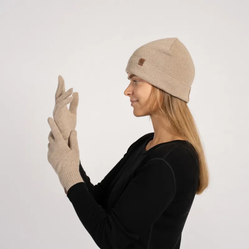 Woman wearing a creamy beige cashmere beanie and matching short gloves, side profile view, adjusting the glove.