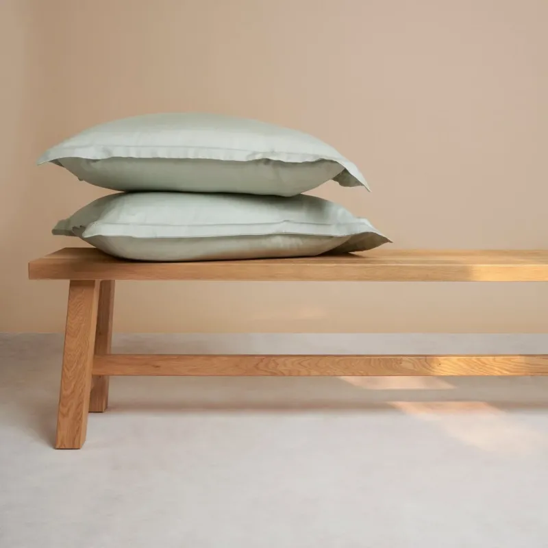 Tencel™ Sateen Pillowcases in Gray Green, stacked on a wooden bench